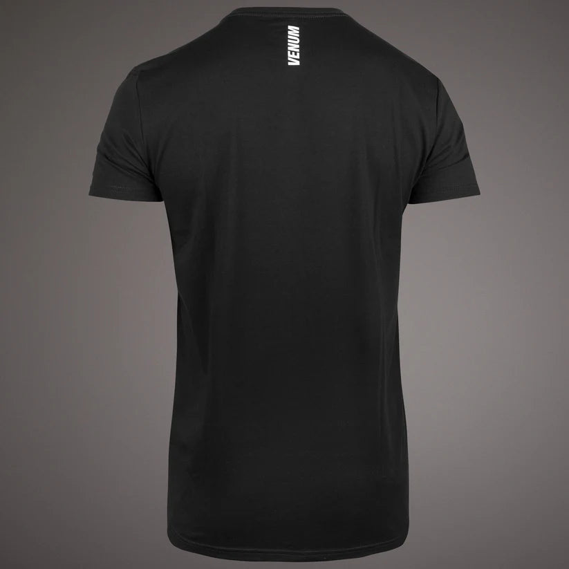Black short-sleeve crewneck t-shirt shown from the back, featuring a vertical white Venum logo printed on the upper back, set against a dark gray gradient background.