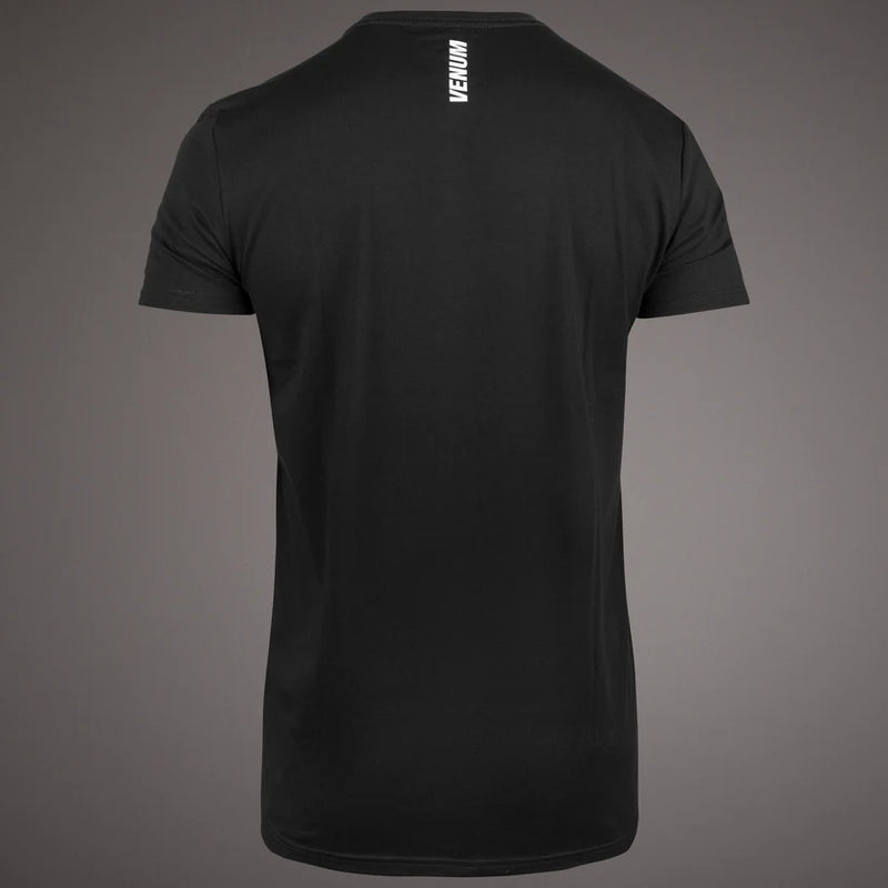 Black short-sleeve crewneck t-shirt shown from the back, featuring a vertical white Venum logo printed on the upper back, set against a dark gray gradient background.