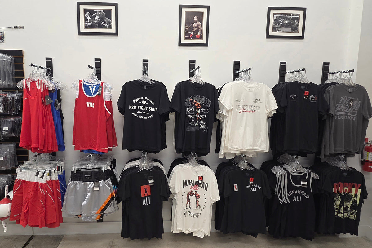 Display of t-shirts and dresses on hangers against a white wall with framed pictures.
