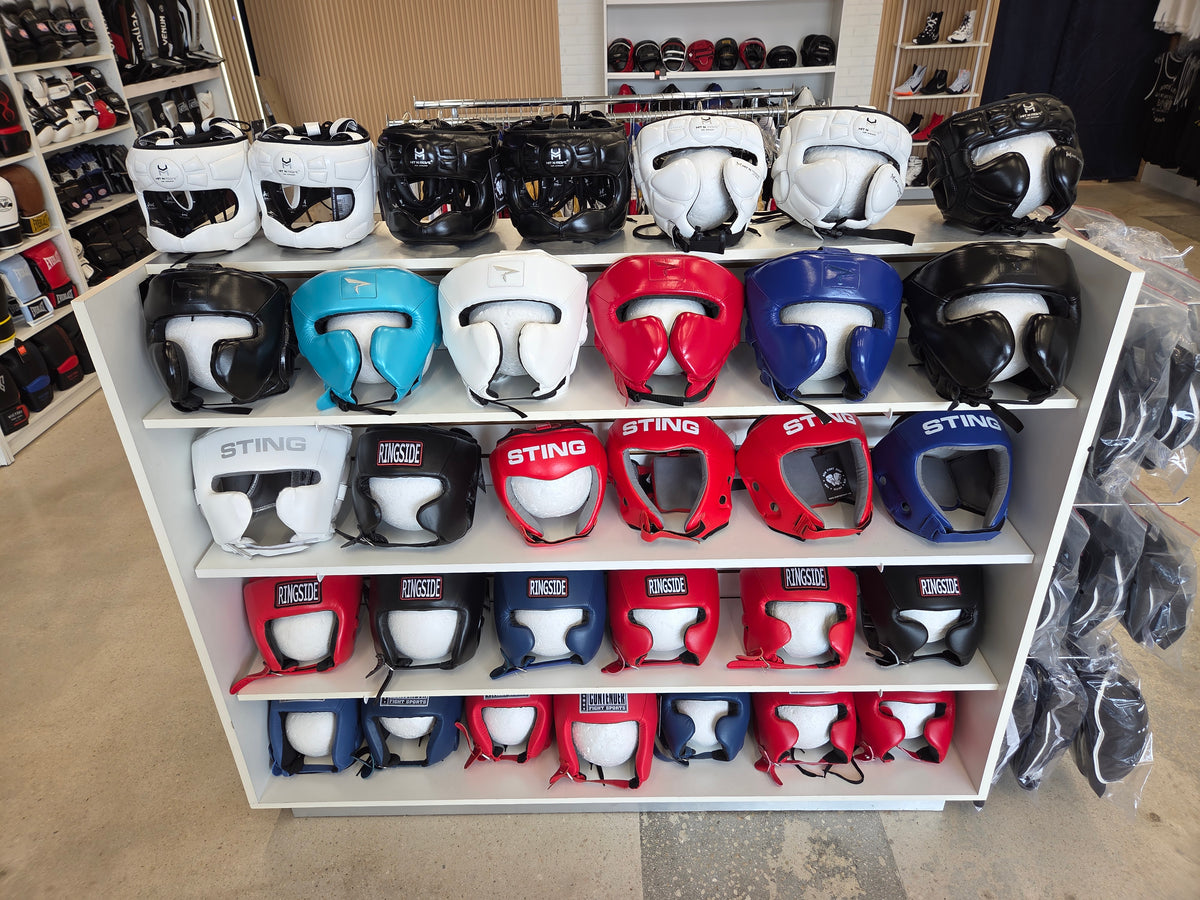 Display of various colored boxing helmets on shelves with 'Sting' branding.