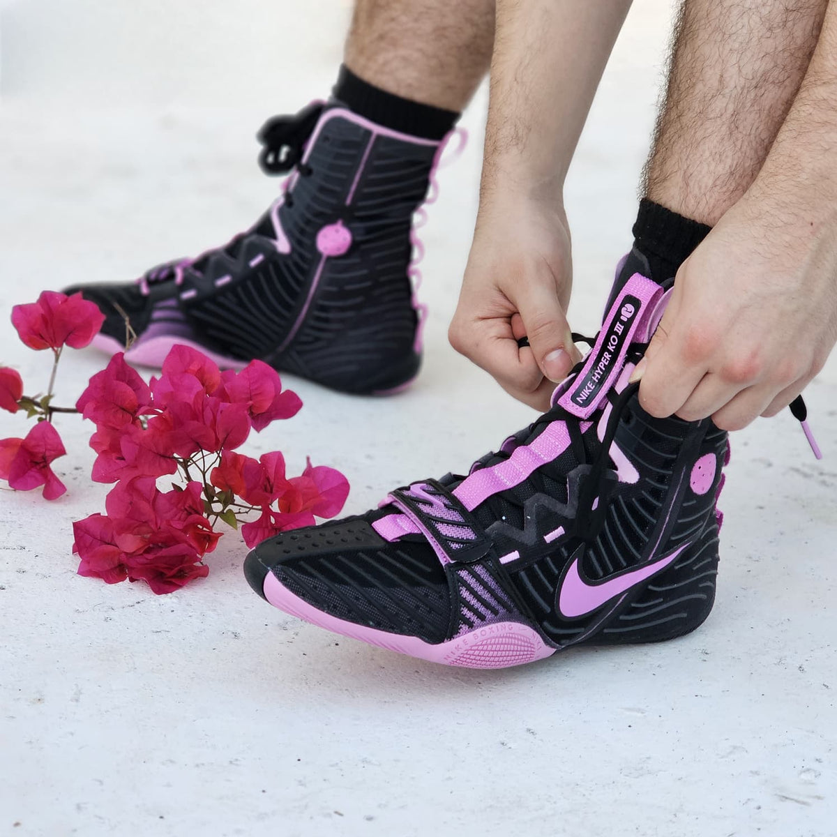 Person tying a black and pink sneaker with flowers on a light background