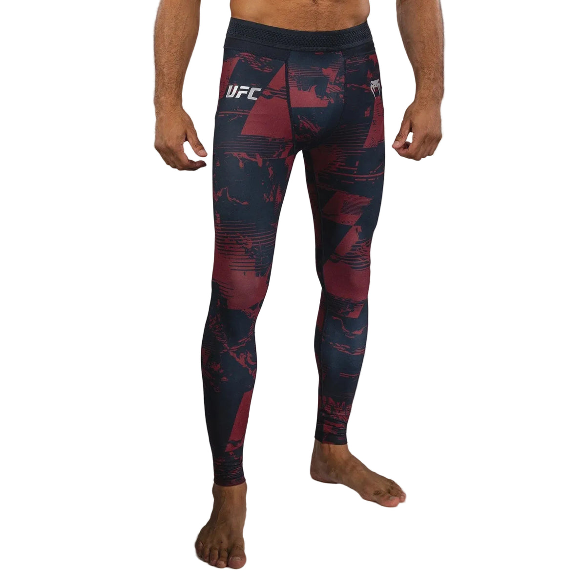 A man wearing UFC athletic tights with a dark navy and red abstract pattern, shown from the waist down against a gray studio background.