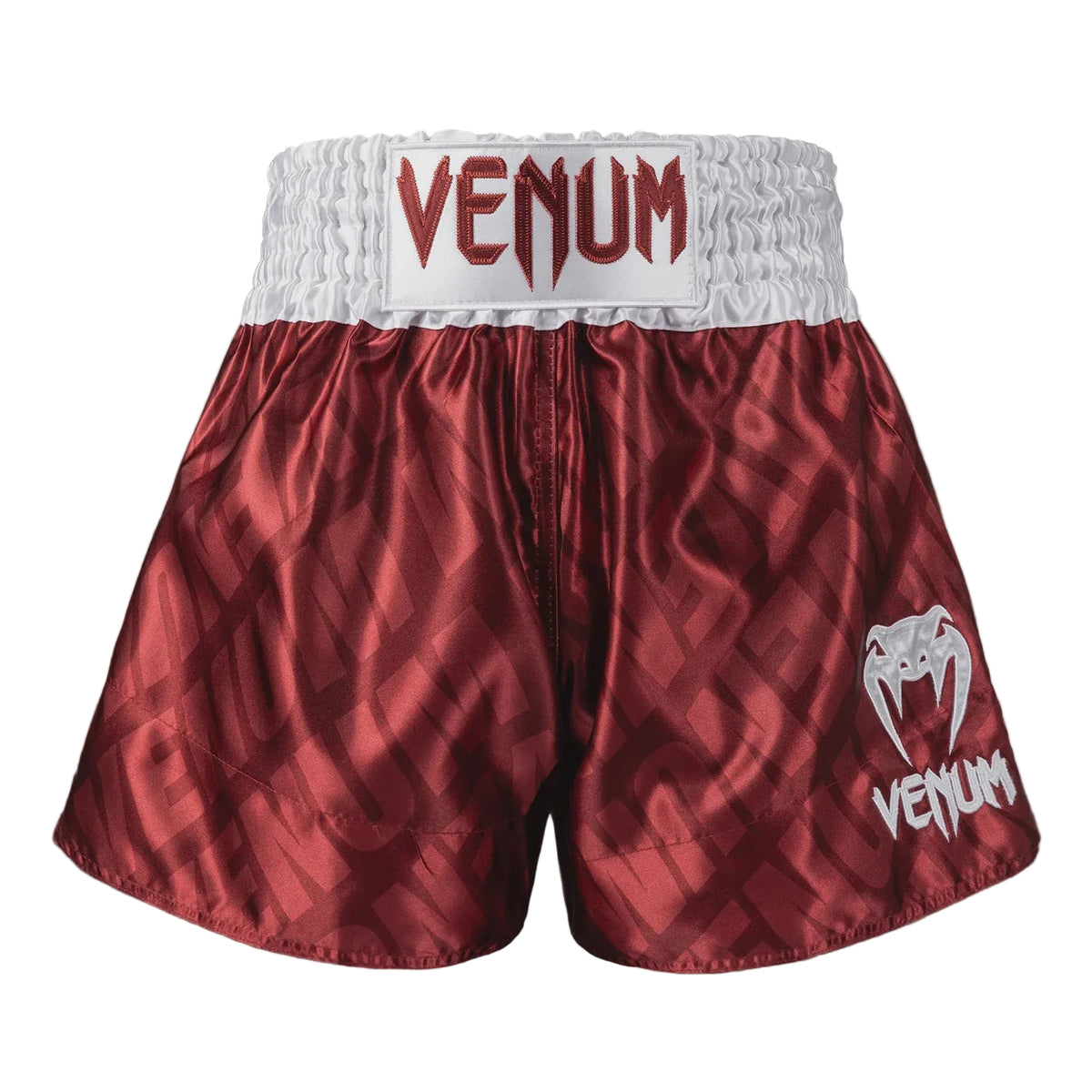Red and white Venum boxing shorts with a textured geometric pattern, featuring a white waistband with red Venum branding and a white logo on the left leg.