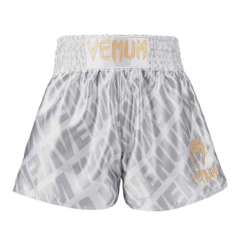 White boxing shorts with gold 'Venum' branding on a gray background