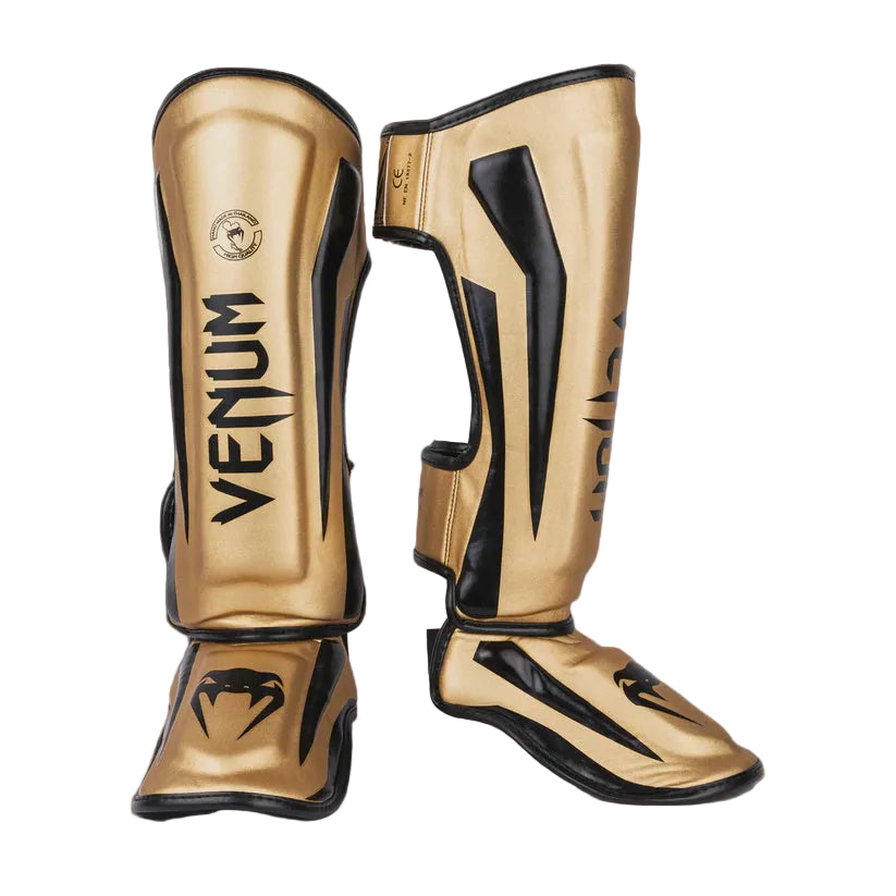 Gold and black Venum shin guards on a gray background