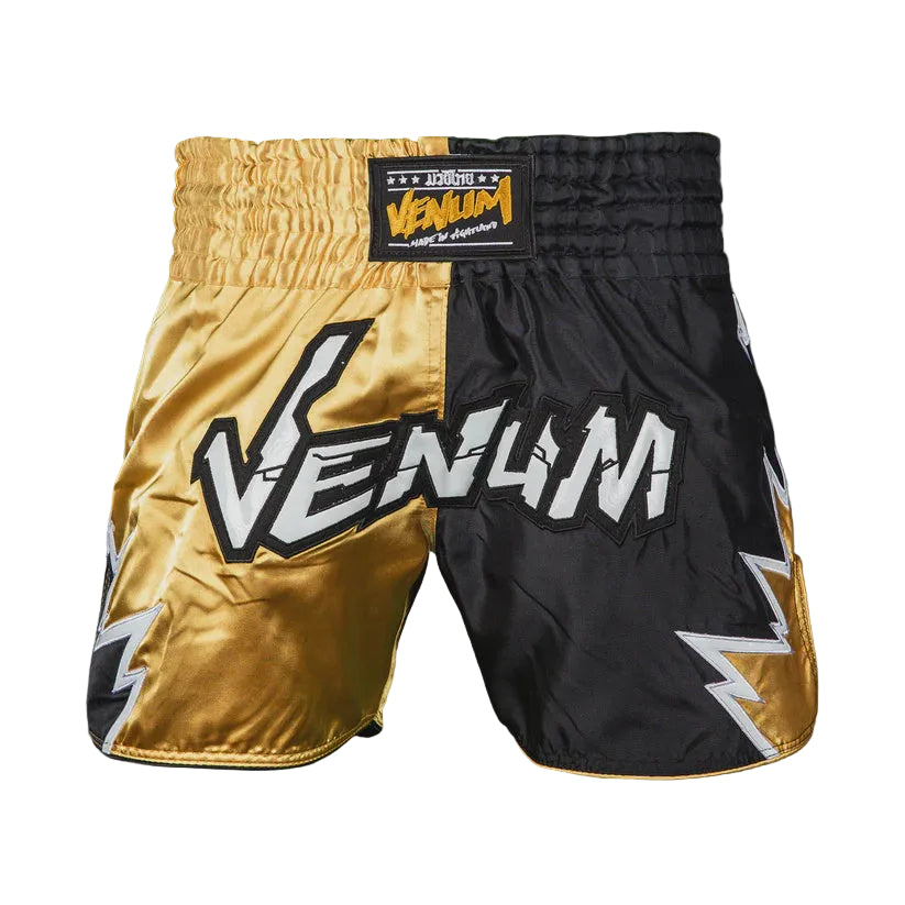 Gold and black boxing shorts with Venum branding on a dark background