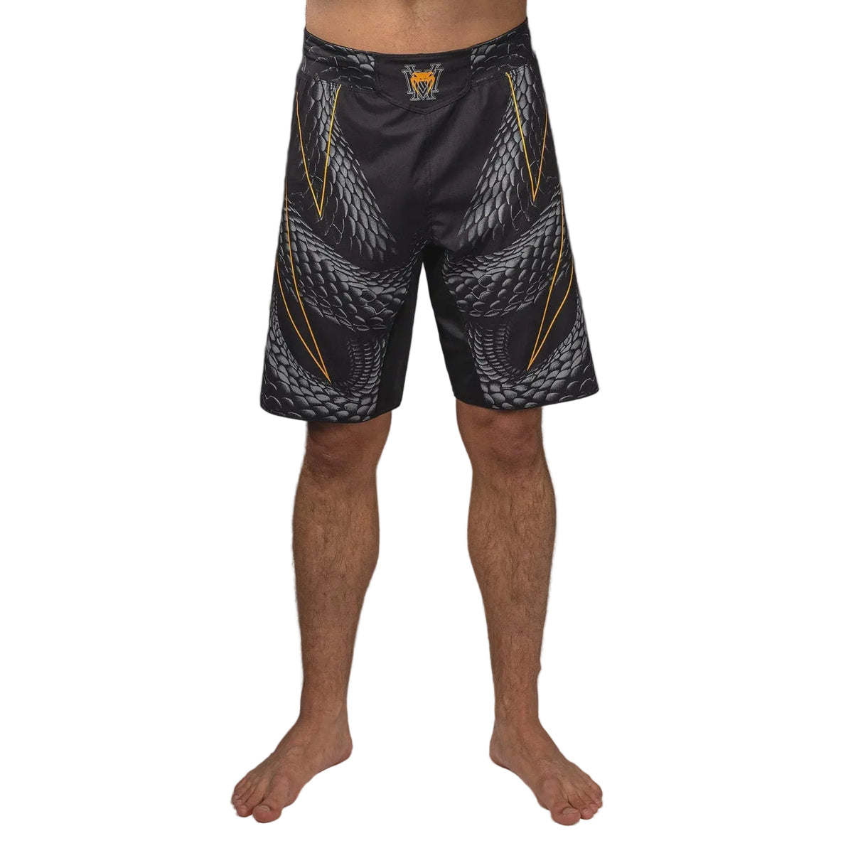 A person standing barefoot against a dark gray studio background wearing athletic shorts with a black base and a gray and yellow abstract pattern.