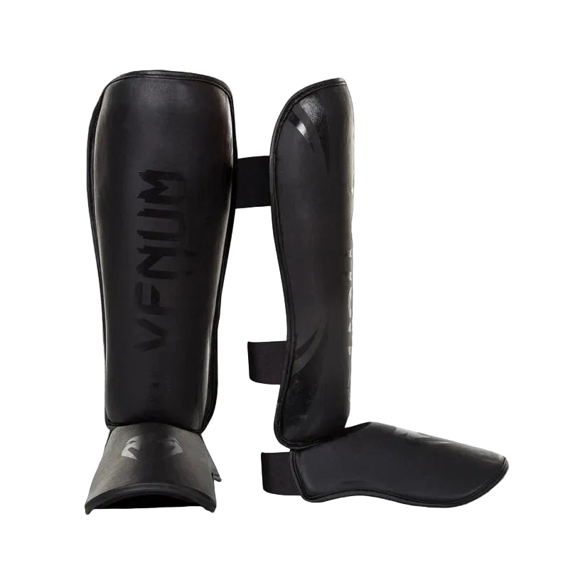 Black Venum shin guards on a gray background