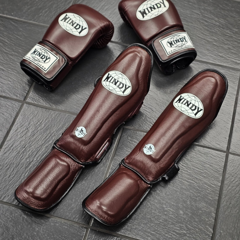 Brown boxing gloves and shin guards with 'Windy' branding on a gray tiled floor.